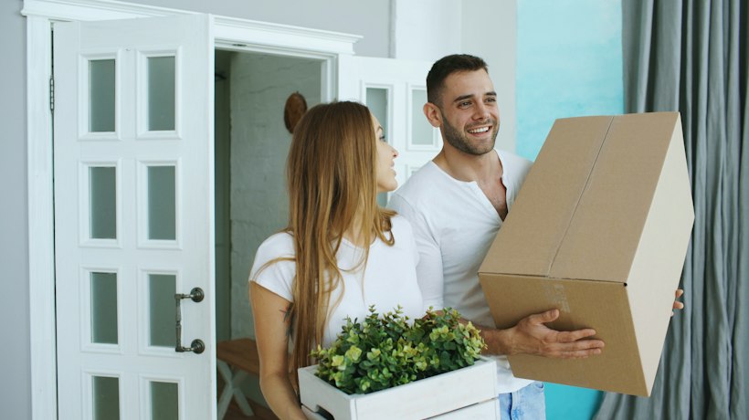 A man carrying a moving box into a bright new home